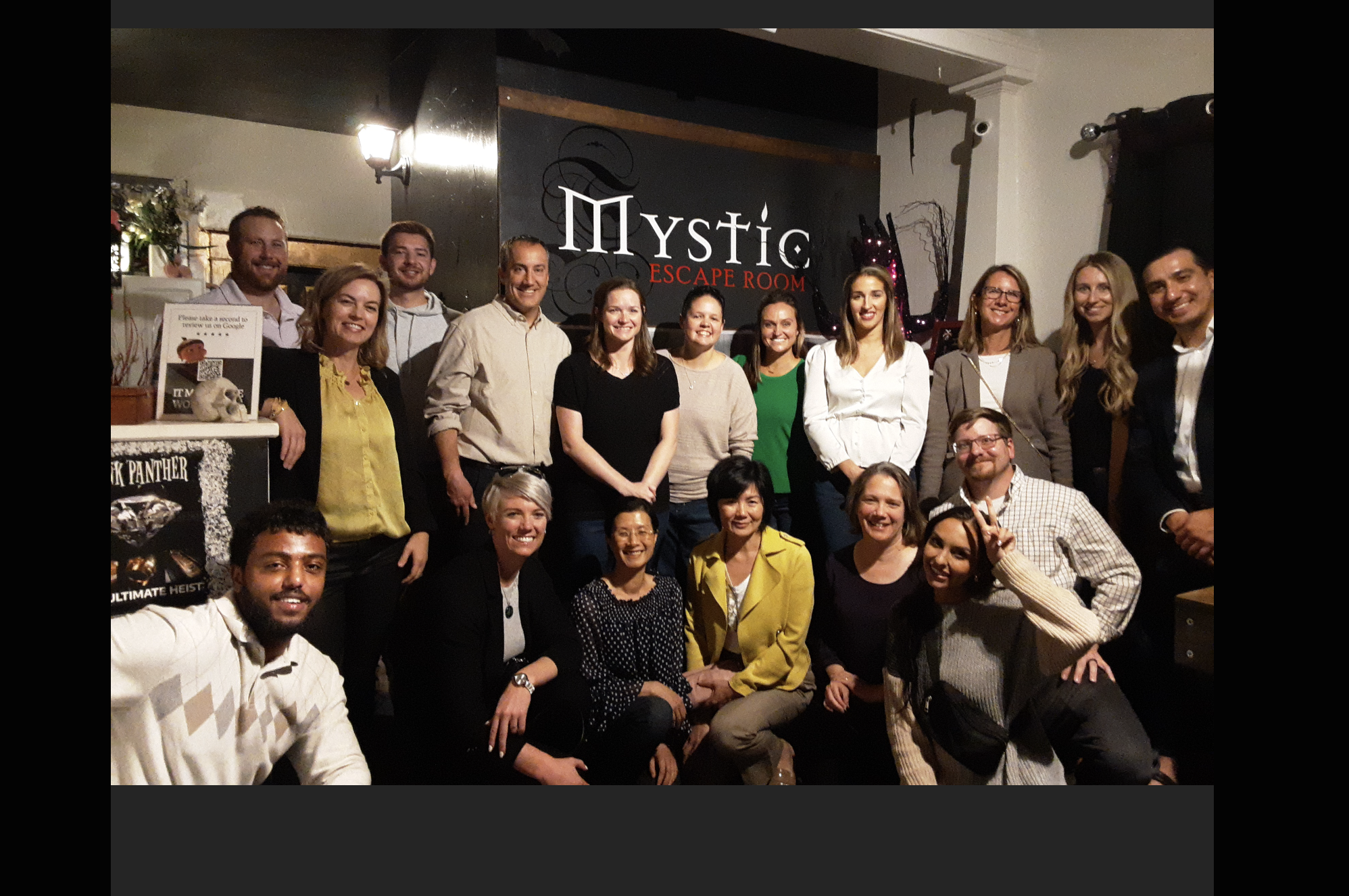 Smiling team gathered in front of the Mystic Escape Room logo at Littleton